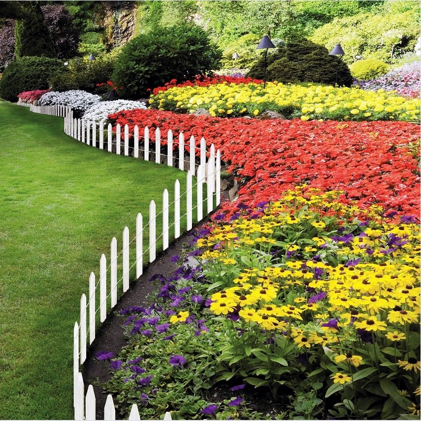 Fehér shtaketinből készült dekoratív kerítés, gyönyörűen kombinálva egy színes virágágyással